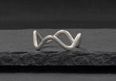 Minimalist wave ring from Hill to Street seating on a dark grey stone over black background